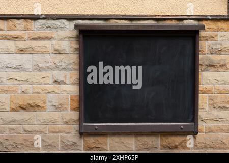 Eine schwarze Inschriftstafel hängt an einer Steinmauer. Schwarze Tafel an einer alten Steinmauer. Stockfoto