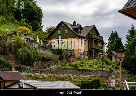 Ein Haus mit einem grünen Dach liegt auf einem Hügel. Das Haus ist von einem üppig grünen Garten umgeben und hat eine große Terrasse. Der Himmel ist bewölkt und gibt den Stockfoto