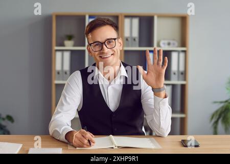 Glücklicher, lächelnder junger Geschäftsmann, der mit der Hand winkt und Hallo beim Online-Videoanruf sagt. Stockfoto