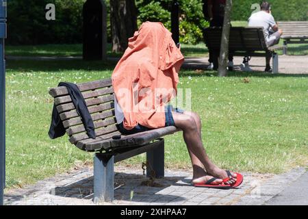 Mann, der auf einer Parkbank sitzt und den Kopf mit einem Hemd bedeckt hat, England, Großbritannien. Konzept: Obdachlose, Obdachlosigkeit, illegale Einwanderer, Einwanderer Stockfoto