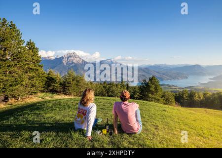 Frankreich, Hautes-Alpes, Saint-Apollinaire, ein Paar, das auf einer Wiese sitzt, genießt das Panorama des Serre-Ponce-Sees von den Höhen von Saint-Apo aus Stockfoto