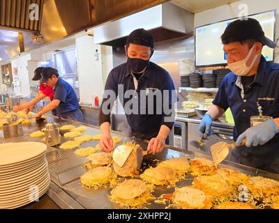 Die Köche bereiten Okonomiyaki, bekannt als Hiroshima’s Soul Food, zu und servieren in rund 2.000 Restaurants in und um die Stadt. Okonomiyaki erschien erstmals nach dem Zweiten Weltkrieg als billiges, füllendes Nahrungsmittel, um den Hunger der Arbeiter zu stillen. Das Gericht besteht aus Schweinefleisch, Eiern und Soba-Nudeln. Der Pfannkuchen besteht aus einer dünnen, krepeartigen Grundschicht und ist mit Zutaten gefüllt. Er wird auf einer langen, flachen Grillplatte gekocht. Die Pastete enthält getrocknete grüne Algenflocken, grüne Zwiebeln, Sojasprossen und Kohl. Japan. Stockfoto