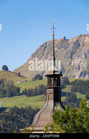 Ein hoher Kirchturm mit Kirchturm steht vor einem Berg. Der Himmel ist klar und blau, und die Bergkette im Hintergrund ist mit t bedeckt Stockfoto