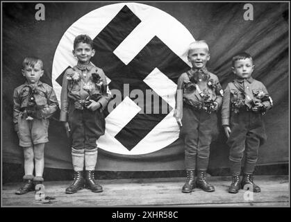 1930er Jahre HAKENKREUZ HITLERJUGEND 4 junge Hitlerjugend-Jungen 4-6 Jahre in Uniform, posieren mit dem Hakenkreuz-Fahnenbanner hinten. Politische Ideologie Nationalsozialismus Indoktrination deutscher Kinder im Nationalsozialismus 1935 Stockfoto