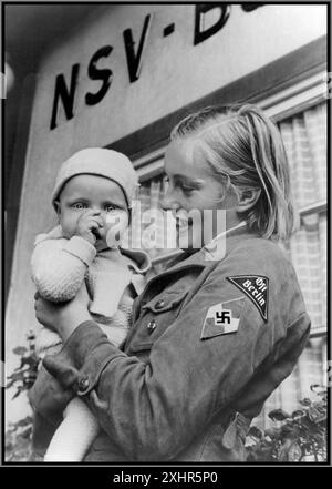 Nazi-Deutschland-Propagandabild von BDM blondes arisches Mädchen in Uniform mit Hakenkreuzabzeichen und Ost-Berlin-Armabzeichen 1939 vor dem NS-Volkswohlfahrtsamt NSV Berlin Nazi-Deutschland aus den 1930er Jahren. Der Bund Deutscher Mädel (kurz BDM) war der Mädchenflügel der Jugendbewegung der NSDAP, der Hitlerjugend. Sie war die einzige legale Jugendorganisation in Nazi-Deutschland. Stockfoto