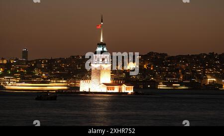 Langzeitaufnahme des Mädchenturms - Kız Kulesi in Istanbul. Die unscharfe Bewegung eines Bootes auf dem Wasser verleiht der Nacht ein dynamisches Element. Stockfoto