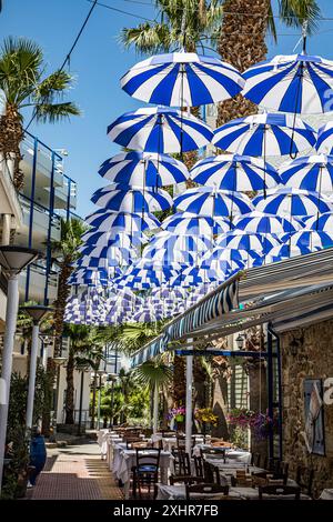 Clevere Verwendung von hübschen blauen und weißen Regenschirmen als Schatten in einem hübschen Restaurant in Heronnissos, kreta, griechischen Inseln. Stockfoto