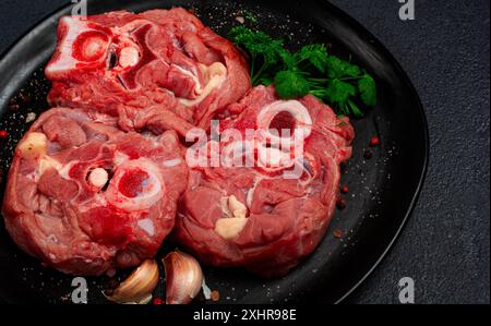 Rohes Steak, Kalbhals auf den Knochen, frisches Fleisch, auf einem schwarzen Teller, Blick von oben, keine Leute Stockfoto