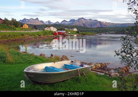 Ein verlassenes Boot liegt an einem grasbewachsenen Ufer mit Bergen und Häusern im Hintergrund, Saltstraumen, Nordland, Norwegen Stockfoto