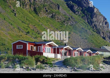 Rote Ferienhütten am Strand vor grünen Bergen an einem sonnigen Tag, Naturlandschaft, Ramberg, Flakstad, Lofoten, Nordland, Norwegen Stockfoto