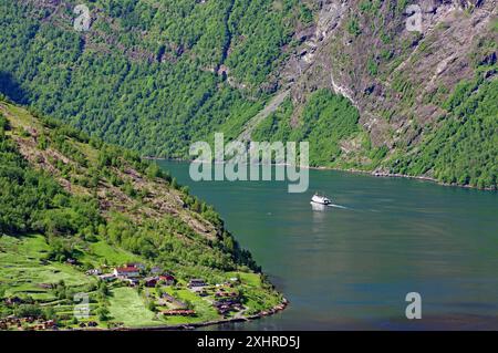 Fjordlandschaft mit einem Schiff umgeben von grünen Bergen und einem kleinen Dorf in Skandinavien, Geiranger, Geirangerfjord, Fjordland, Norwegen Stockfoto