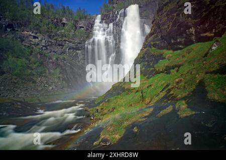 Malerischer Wasserfall, der über Felsen in einen Fluss stürzt, umgeben von üppigem Grün und Wald im Hintergrund, Regenborgen, Skjervefossen, Voss Stockfoto