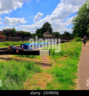 Schmales Boot, das durch die Schleuse auf dem Kennett & Avon Kanal bei Devizes fährt - ein Mann, der auf dem Schleusenmechanismus ruht und darauf wartet, dass das Schleusenschloss läuft. Juli 2024. Sommer. Stockfoto