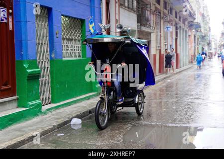 Havanna, Kuba, Zentralamerika, ein Mann, der eine Rikscha auf einer nassen Straße in einer städtischen Umgebung fährt Stockfoto