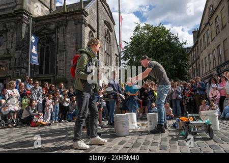 Straßenmusiker umgeben von Zuschauern, die auf leeren Eimern trommeln, das größte Kulturfestival der Welt, The Fringe, High Street, Edinburgh, Schottland Stockfoto