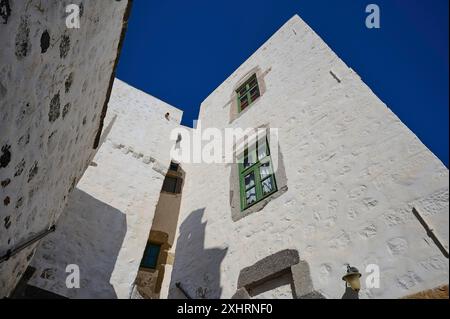 Blick nach oben auf ein traditionelles weißes Gebäude mit grünen Fenstern und architektonischen Details unter klarem Himmel, Kloster der Apokalipsis, Patmos Stockfoto