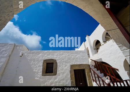 Blick von unten auf weiße Gebäude und eine Treppe unter einem Bogen im griechischen Kloster, im Inneren des Klosters, Agiou Theologou Kloster, Chora Stockfoto