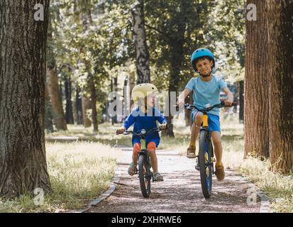 Glückliche Kinder, die am heißen Sommertag im Stadtpark Fahrrad fahren Stockfoto