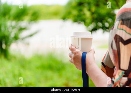 Eine Frau, die mit einem Hund an der Leine läuft und ihre Tasse Kaffee trinkt Stockfoto