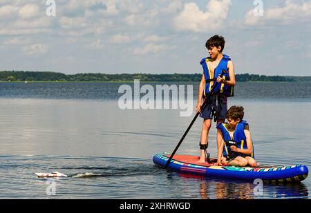 Kinder auf einem SUP-Paddleboard auf dem See spielen mit einem RC-Modellboot. Stockfoto