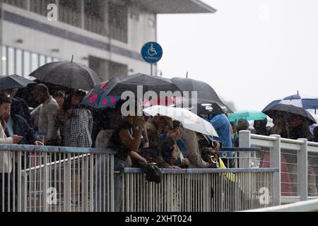 Windsor, Berkshire, Großbritannien. Juli 2024. Nach einem milden Start des abendlichen Rennens gab es heute Abend starken Regen auf der Royal Windsor Racecourse in Windsor, Berkshire. Der Regen hielt die Rennfahrer nicht davon ab, die Rum- und Reggae-Abendrennen zu genießen, während sie unter Regenschirmen saßen und im Regen im echten britischen Stil nach Essen warteten. Eine Wetterwarnung für MET Office Yellow bleibt bis morgen, 16. Juli 09,00, bei starkem Regen bestehen. Quelle: Maureen McLean/Alamy Live News Stockfoto