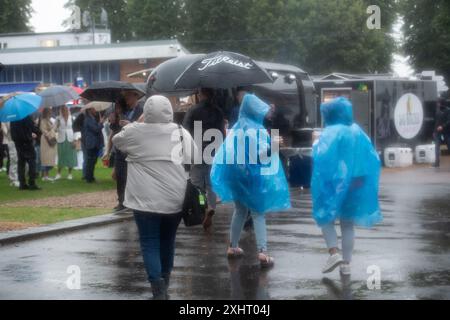 Windsor, Berkshire, Großbritannien. Juli 2024. Nach einem milden Start des abendlichen Rennens gab es heute Abend starken Regen auf der Royal Windsor Racecourse in Windsor, Berkshire. Der Regen hielt die Rennfahrer nicht davon ab, die Rum- und Reggae-Abendrennen zu genießen, während sie unter Regenschirmen saßen und im Regen im echten britischen Stil nach Essen warteten. Eine Wetterwarnung für MET Office Yellow bleibt bis morgen, 16. Juli 09,00, bei starkem Regen bestehen. Quelle: Maureen McLean/Alamy Live News Stockfoto