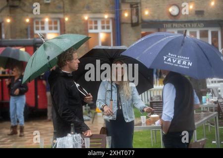 Windsor, Berkshire, Großbritannien. Juli 2024. Nach einem milden Start des abendlichen Rennens gab es heute Abend starken Regen auf der Royal Windsor Racecourse in Windsor, Berkshire. Der Regen hielt die Rennfahrer nicht davon ab, die Rum- und Reggae-Abendrennen zu genießen, während sie unter Regenschirmen saßen und im Regen im echten britischen Stil nach Essen warteten. Eine Wetterwarnung für MET Office Yellow bleibt bis morgen, 16. Juli 09,00, bei starkem Regen bestehen. Quelle: Maureen McLean/Alamy Live News Stockfoto