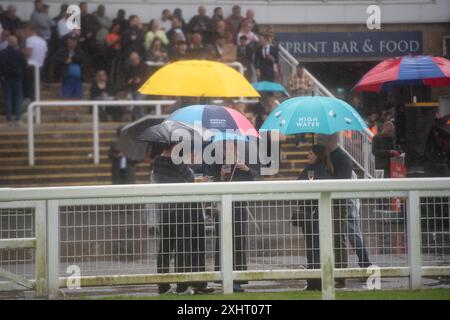 Windsor, Berkshire, Großbritannien. Juli 2024. Nach einem milden Start des abendlichen Rennens gab es heute Abend starken Regen auf der Royal Windsor Racecourse in Windsor, Berkshire. Der Regen hielt die Rennfahrer nicht davon ab, die Rum- und Reggae-Abendrennen zu genießen, während sie unter Regenschirmen saßen und im Regen im echten britischen Stil nach Essen warteten. Eine Wetterwarnung für MET Office Yellow bleibt bis morgen, 16. Juli 09,00, bei starkem Regen bestehen. Quelle: Maureen McLean/Alamy Live News Stockfoto