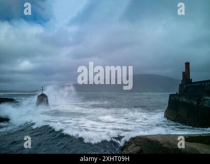 Stürmische Meere treffen das Kreuz im Purteen Harbour auf Achill Island, County Mayo, Irland, wo 1922 der Film „The Banshees of Inisherin“ gedreht wurde. Stockfoto