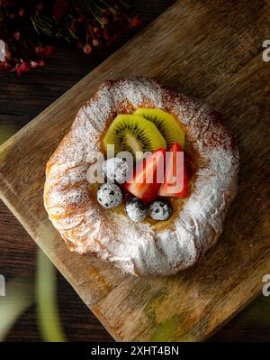 Frisch gebackenes dänisches Gebäck mit Marmelade und Obst darüber. Dunkler Holzhintergrund. Stockfoto