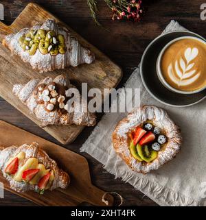 Frisch gebackene Gourmet-Croissants und Blätterteig mit Beeren, Marmelade, Schokolade und Pistazien. Cappuccino-Tasse auf dunklem Holzhintergrund. Draufsicht. Stockfoto