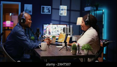 Content Creator hat während des Podcasts gute Gespräche mit Gästen. Gastgeber genießt Kaffee zusammen mit einer fröhlichen Frau live im Apartmentstudio während der Internetshow, Zoom out shot Stockfoto