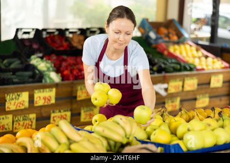 Verkäuferin, die im Supermarkt arbeitet und Äpfel auf der Theke verteilt Stockfoto