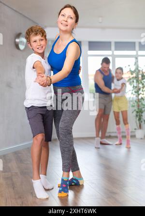 Glückliche Mutter und Sohn, die zusammen mit anderen Familienmitgliedern Tanzen üben Stockfoto