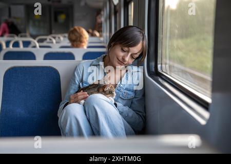 Glückliche lächelnde Frau mit süßem flauschigen Kätzchen, die gemeinsam reisen, mit einem elektrischen Zug fahren. Stockfoto