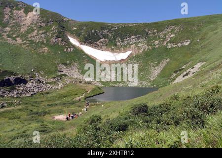 REGION ZAKARPATTIEN, UKRAINE - 14. JULI 2024 - Touristen werden am höchsten Bergsee der Ukraine, Brebeneskul, gesehen, wo trotz der Temperatur von 35°C der Schnee noch nicht geschmolzen ist, im Karpaten-Biosphärenreservat, Bezirk Rakhiv, Region Zakarpattien, Westukraine Stockfoto