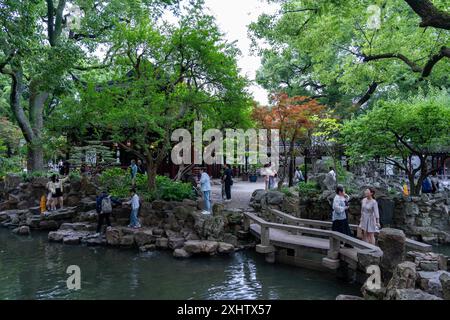 Shanghai, China - 06. Juni 2024 : Eine Steinbrücke überquert einen Teich im ruhigen Yu Garden, Shanghai, umgeben von üppigem Grün und lebhaften Blumen. Stockfoto