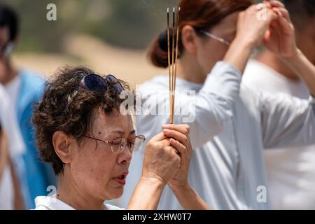 Sanya, Hainan Island, China - 17. Mai 2024: Alte Frau, die im chinesischen Tempel rauchende Räucherstäbchen hält Stockfoto
