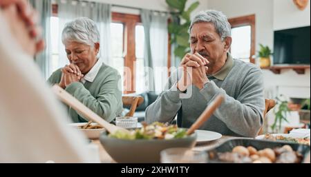 Seniorenpaar, Essen und Gebet zu Hause mit der Familie, Segen und Dankbarkeit für das Essen im Speisesaal. Ältere Menschen, glaube und Augen geschlossen am Tisch Stockfoto