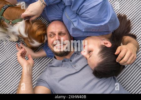 Fröhliche Familie erwartet ein Baby. Ein Mann und seine schwangere Frau mit Hund liegen auf Gras in einem Stadtpark. Blick von oben. Schwangerschaft, erwartet ein Baby, Schatz Stockfoto