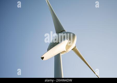 Dieses Bild zeigt eine Nahaufnahme einer modernen Windturbine mit niedrigem Winkel vor einem klaren blauen Himmel. Das schlanke, aerodynamische Design des b Stockfoto