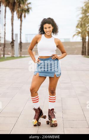 Portrairt einer jungen lächelnden Frau mit Rollschuhen, die ihre Zeit in einem urbanen Park mit Palmen im Hintergrund genießt. Stockfoto