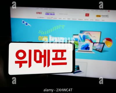 Person mit Smartphone und Logo des südkoreanischen E-Commerce-Unternehmens Wemakeprice vor der Website. Schwerpunkt auf dem Display des Telefons. Stockfoto