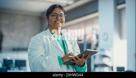 Porträt einer jungen indischen Spezialistin in einem Labormantel lächelnd und mit Laptop-Computer. Professionelle und erfolgreiche Frau, die als Ingenieurin arbeitet, denkt und High-Tech-Projekte entwickelt Stockfoto