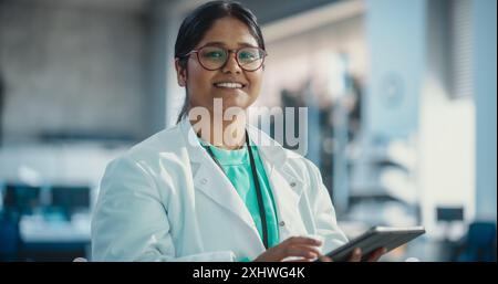 Porträt einer indischen jungen Wissenschaftlerin mit digitalem Tablet-Computer, Blick auf die Kamera und Lächeln in einem Labor. Selbstbewusste professionelle Frau, die als Ingenieurin und Überwachungstechnologie-Projekte arbeitet Stockfoto