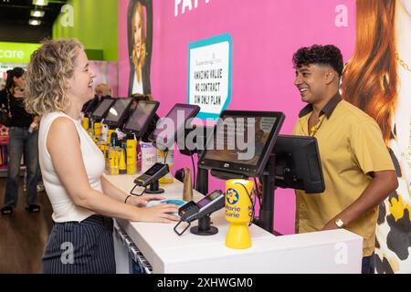 Der Schauspieler Karim Zeroual mit einem Kunden bei der Einführung der Gelb-Pfennige-Spendeninitiative in Superdrug, Manchester, drängte die Käufer, ihre Einkäufe um 20 Pent aufzustocken, um für die wichtige Arbeit der führenden britischen End-of-Life-Wohltätigkeitsorganisation zu spenden. Ausgabedatum: Dienstag, 16. Juli 2024. Stockfoto