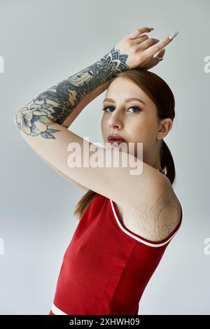 Eine junge Frau mit Tätowierungen auf Armen und Schultern posiert in einem roten Tanktop und kariertem Rock. Stockfoto