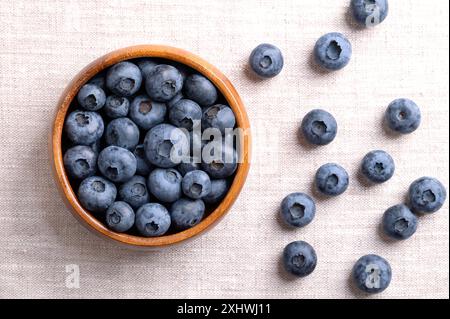 Heidelbeeren in einer Holzschale auf Leinenstoff. Dunkelblaue, reife, rohe Beeren, Früchte von Vaccinium corymbosum, angebaute Heidelbeeren. Stockfoto