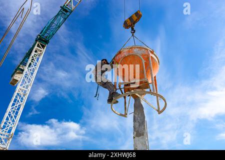 Bauarbeiter entladen konische Metallschaufeln, transportieren und liefern Zementgemische hoch und gießen Beton in eine hohe vertikale Form für den Bau Stockfoto