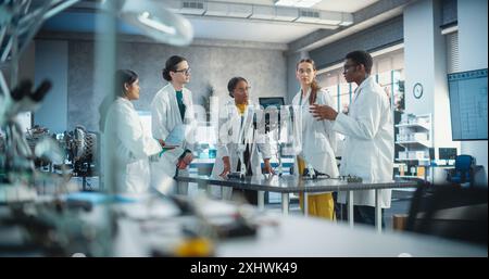 Professionelles junges internationales Team von weiblichen und männlichen Ingenieuren diskutiert industrielle KI Roboterhunde in Factory Development Workshop. Technische Einrichtung mit Maschinen, Computern, Forschungsausrüstung Stockfoto